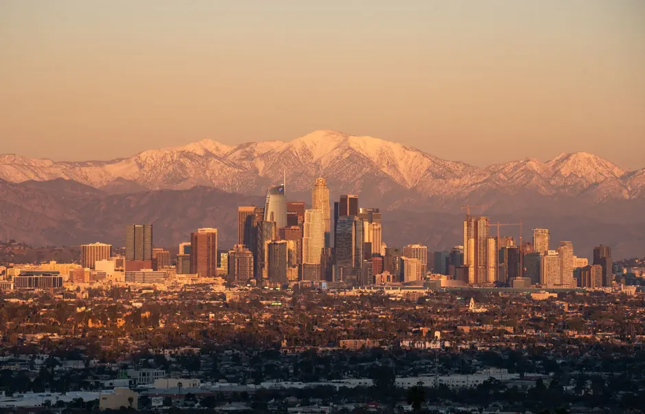 Stunning Los Angeles skyline during golden hour with snow-capped mountains in the background.